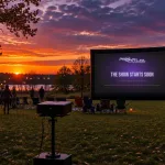 Guests arriving at sunset with lawn chairs as the Pro Stylez Entertainment pre-show slide glows on the inflatable screen