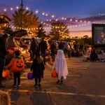 Trunk-or-treat in a parking lot with Scoob! playing on the outdoor movie screen